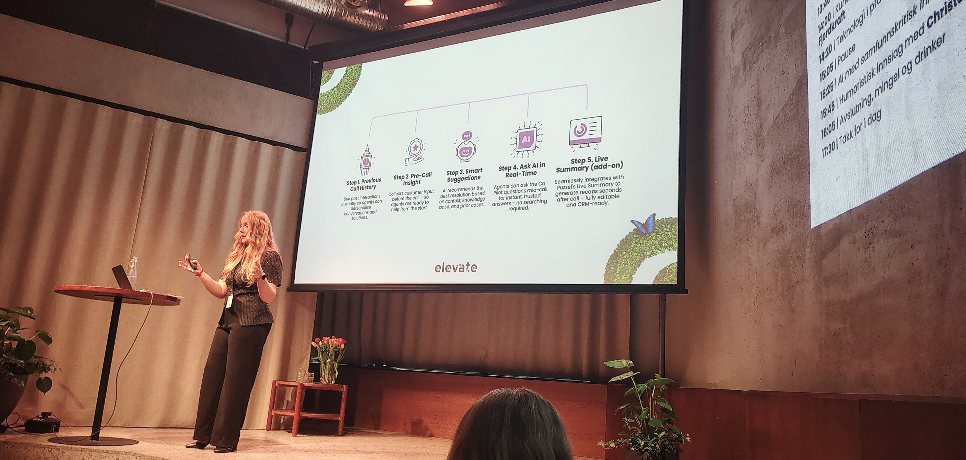 Female talker standing on the scene with a big screen with slides behind her